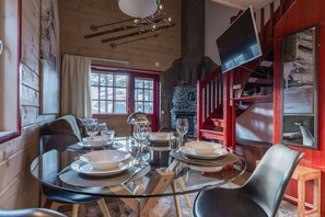 Een eethoek met een ronde glazen tafel voor vier personen, houten stoelen, een stenen open haard en een rode wenteltrap.