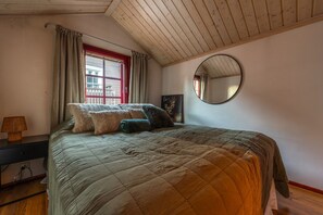Ein Schlafzimmer mit einem Bett, einem Fenster mit Vorhängen, einer Nachttischlampe und einem runden Spiegel an der Wand.