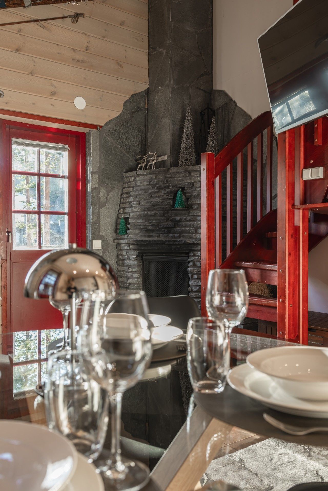 A dining area with a stone fireplace, wooden ceiling, and a red staircase.