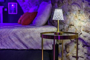 A bed with a red pillow, a lamp on a round table, and a textured wall.