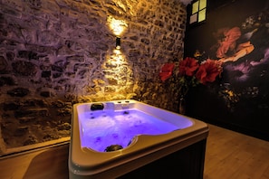 Un muro de piedra con un accesorio iluminado, un jacuzzi con luz morada y una pintura de flores.