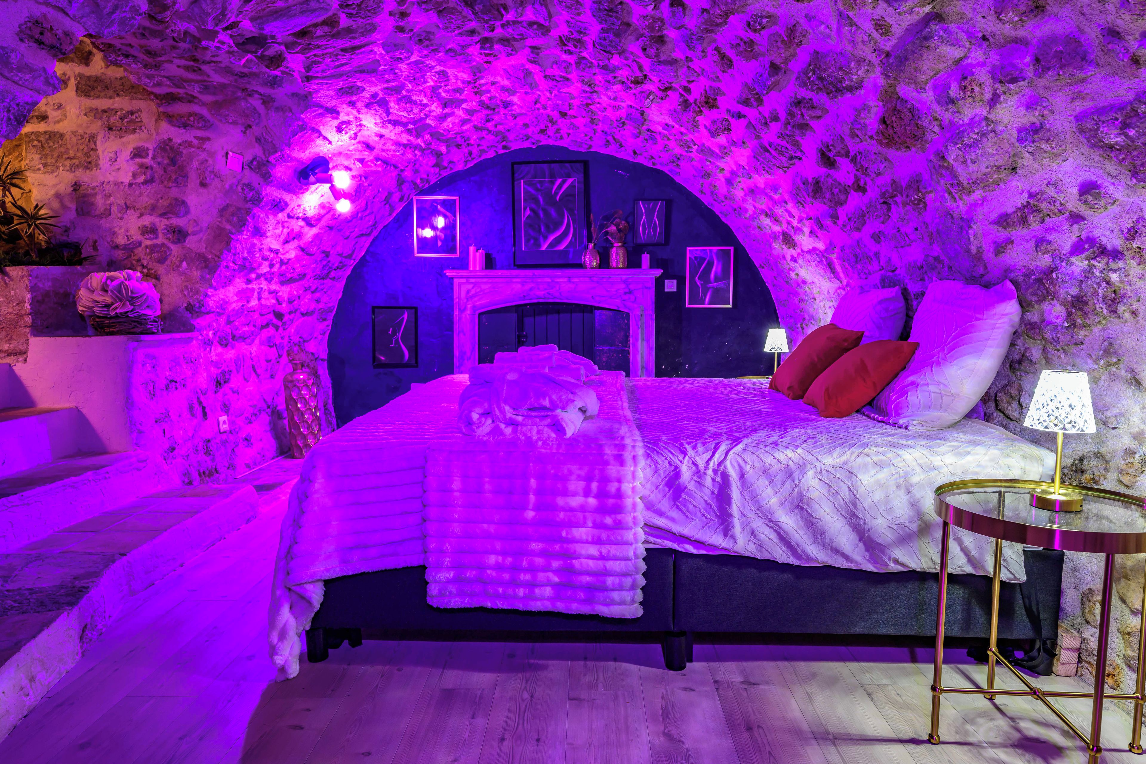 A bedroom with a stone wall, a bed with a headboard, a bedside table, and a lamp.