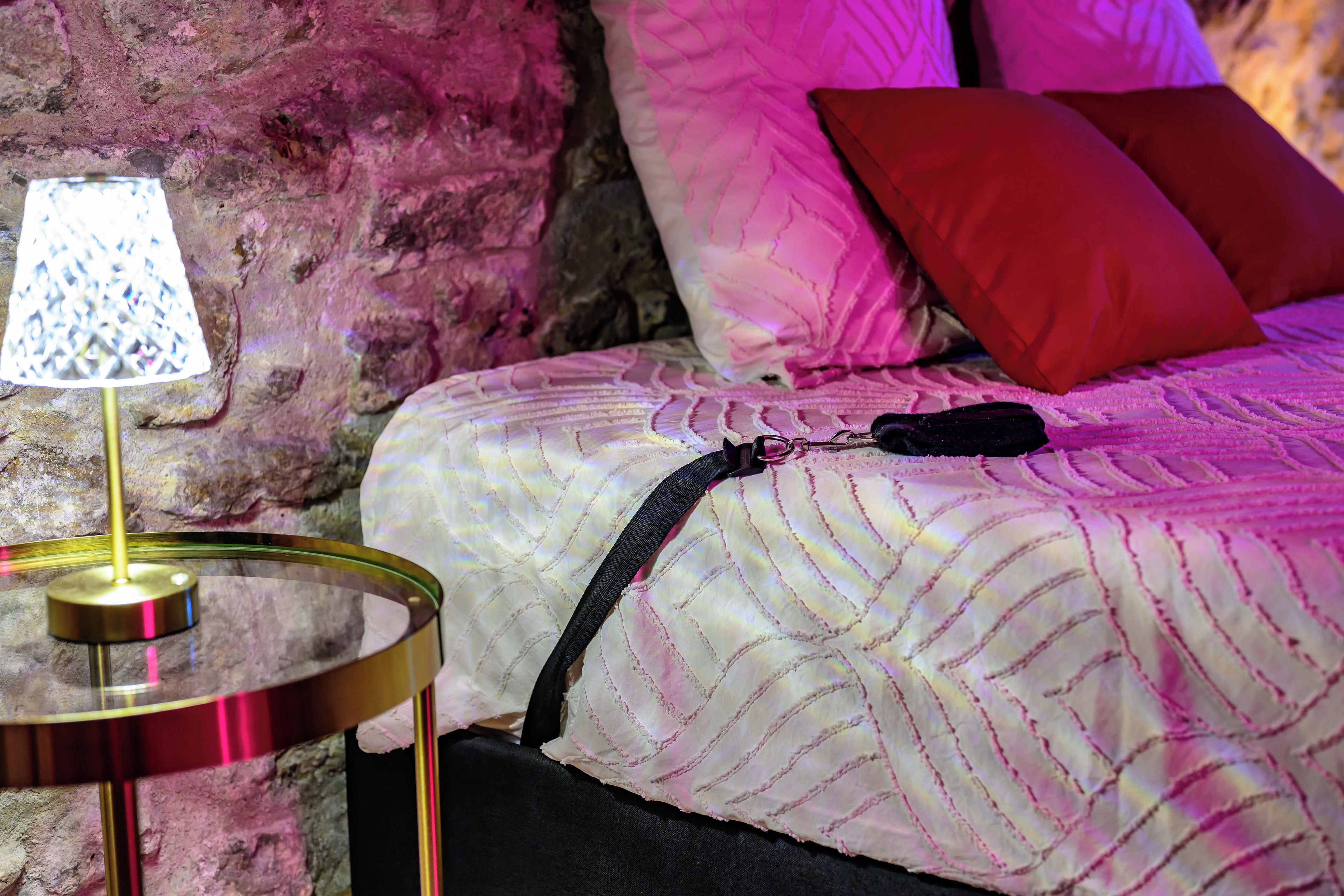 Un lit avec une couvre-lit à motifs, un oreiller rouge et une lampe sur une table de chevet.