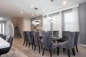A modern dining area with a glass-top table and velvet chairs, a staircase, and a chandelier. - Amazing 9 bedrooms and private pool with spa (Kissimmee)