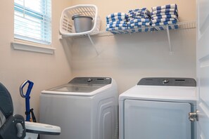 A laundry area with two white washing machines, a blue and white checkered towel on a shelf, and a white laundry basket. - Amazing 9 bedrooms and private pool with spa (Kissimmee)