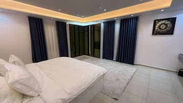 Un dormitorio moderno con cama, un ventanal con cortinas e iluminación empotrada en el techo.