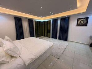 Quarto moderno com cama, uma janela grande com cortinas e iluminação embutida no teto.
