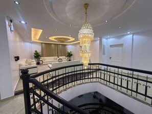 Interior com vários níveis, destacando um lustre imponente, escada com guarda-corrimão preto e área de estar com sofás.