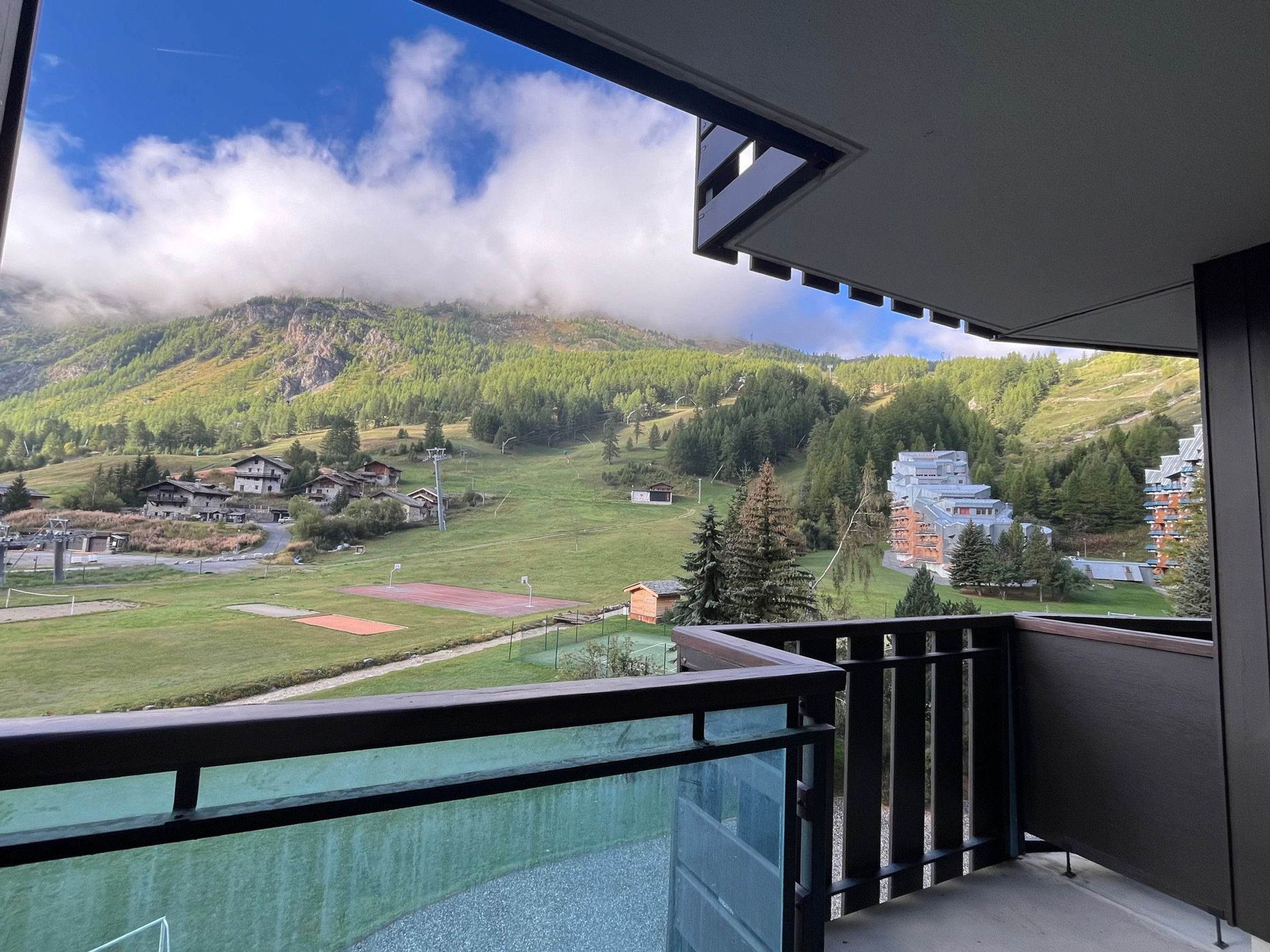 A balcony with a view of a mountainous landscape, including houses and a ski resort.