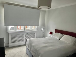 Una camera da letto con un letto, una finestra con persiane, un termosifone e un comodino con una lampada.