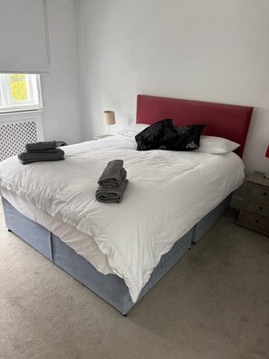 Ein ordentlich bezogenes Bett mit weißer Bettwäsche, einem roten Kopfteil und einer Nachttischlampe.
