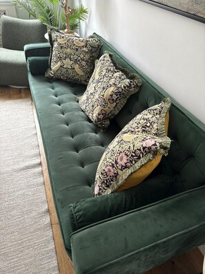 Ein grünes, gepolstertes Sofa mit dekorativen Kissen und einer Pflanze im Topf.