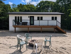 Ein Strandhaus mit einer Terrasse, Sitzgelegenheiten im Freien und einer Feuerstelle.