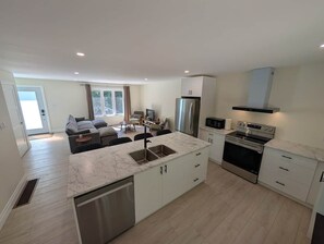 Eine moderne Küche mit einer zentralen Kochinsel, Edelstahlgeräten und einem Essbereich mit einer Couch und Stühlen.