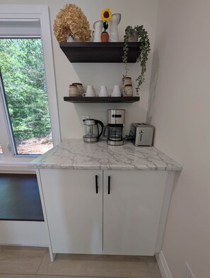Eine Küche mit Marmorarbeitsplatte, einer Kaffeemaschine, einem Toaster und einem Regal mit Dekoration.