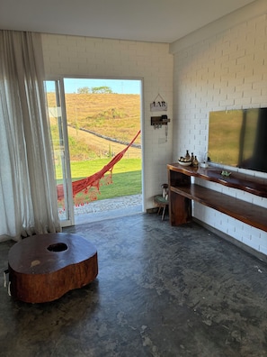 Een moderne woonkamer met een grote televisie, een hangstoel en uitzicht op een groen landschap.