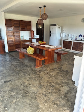 A spacious kitchen with a wooden dining table, a hanging light fixture, and a refrigerator. - Casa Pedra do Cavalo | Swimming pool and Paraguaçu River | Pier and boat ramp (Governador Mangabeira)