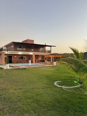 Una casa de dos pisos con balcón, zona de estar exterior y piscina.