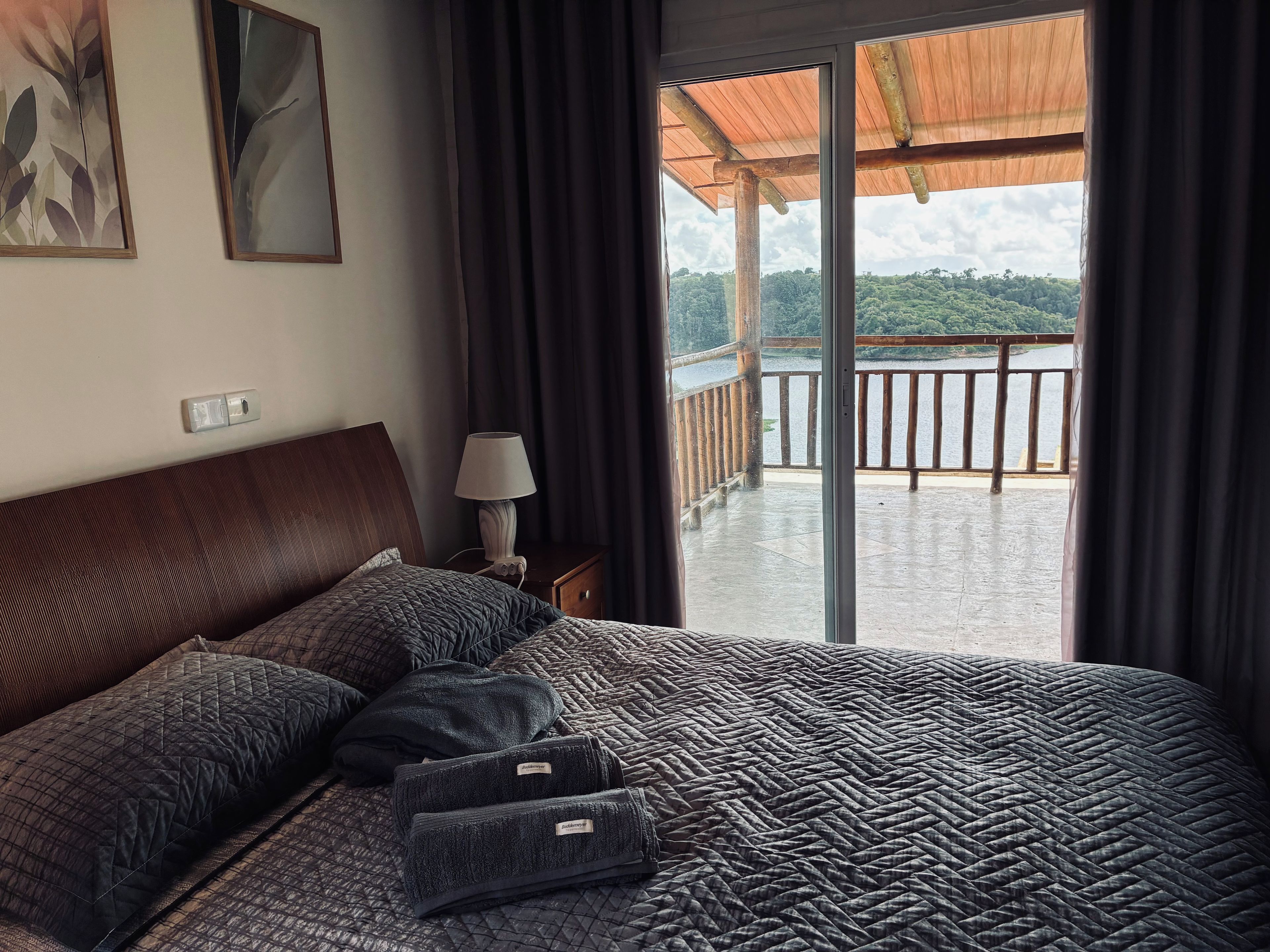 Un dormitorio con una cama grande, una mesita de noche con una lámpara y vistas a un balcón con barandilla.