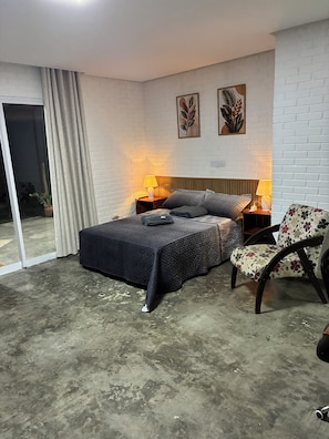 A bedroom with a bed, two bedside lamps, a chair, and a view through a sliding glass door. - Casa Pedra do Cavalo | Swimming pool and Paraguaçu River | Pier and boat ramp (Governador Mangabeira)