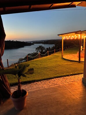 Un patio con vistas a un río, césped y una pérgola de madera con luces.