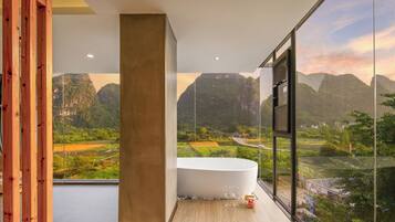 A modern bathroom with a large bathtub, a wooden column, and a view of a mountainous landscape through large windows.