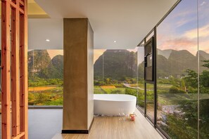 Un baño moderno con una bañera grande, un pilar de madera y vistas a un paisaje montañoso a través de amplios ventanales.