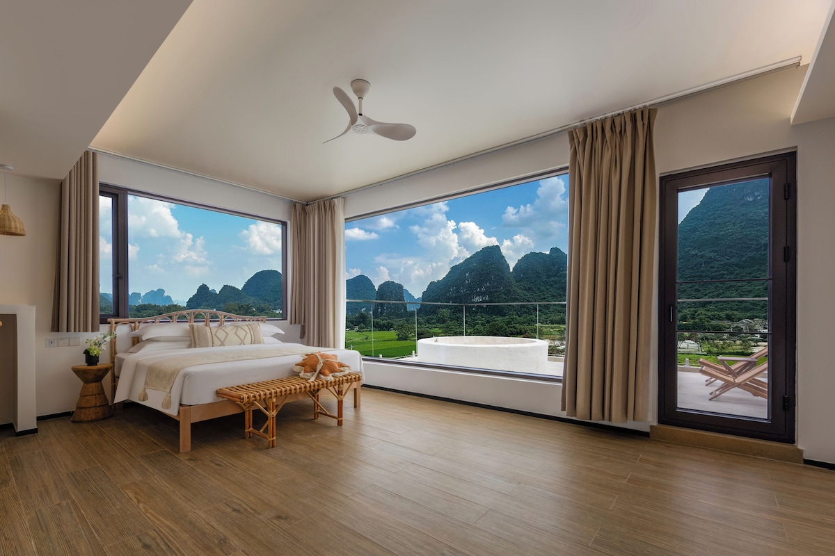 A spacious bedroom with a large bed, a ceiling fan, and a view of a mountainous landscape.
