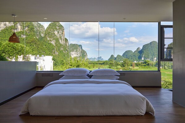 A bedroom with a large bed, a view of green hills and mountains, and a hanging light fixture. - Park Su Qidu Homestay (Guilin)