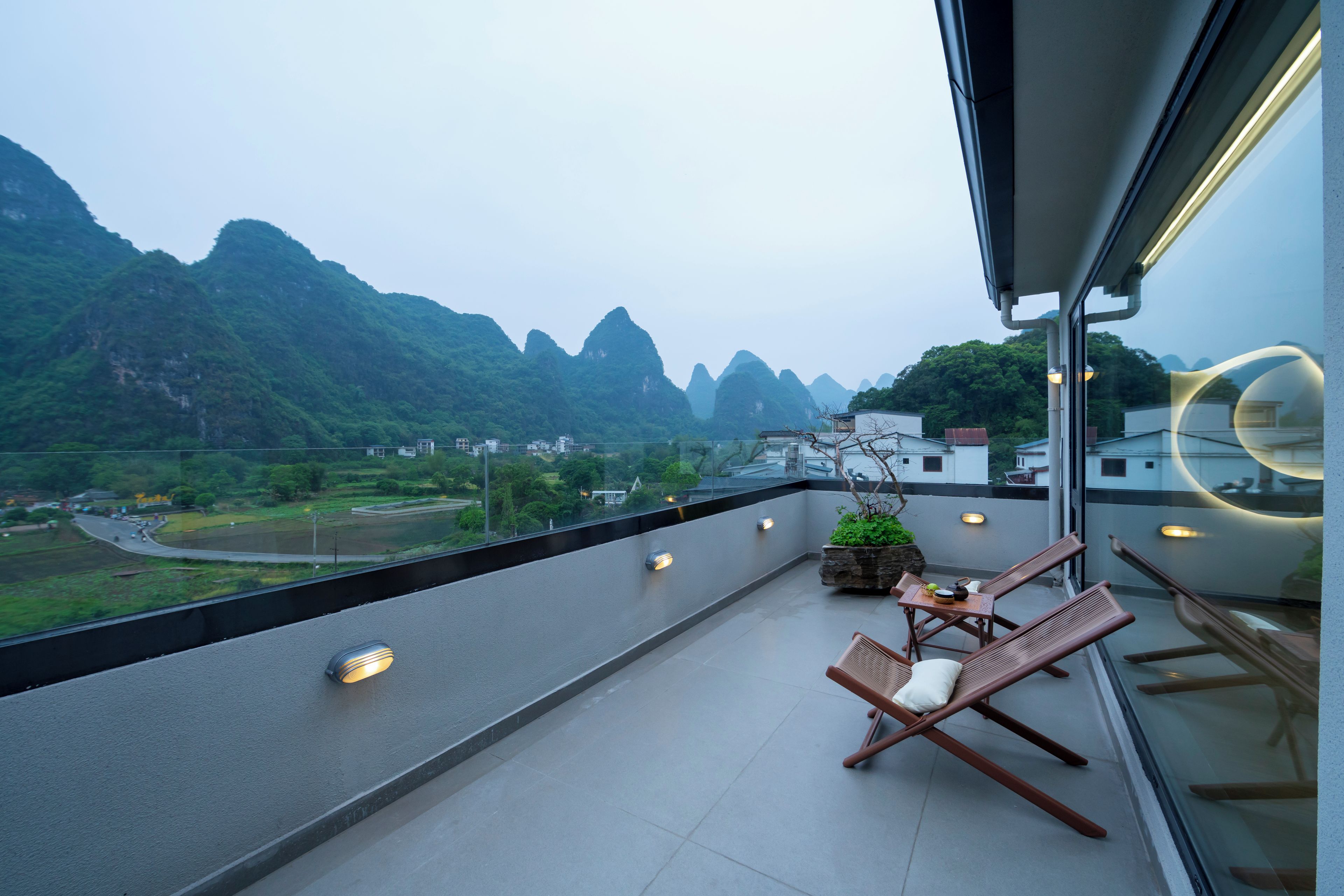 A balcony with a view of mountains, a table with chairs, and a potted plant.