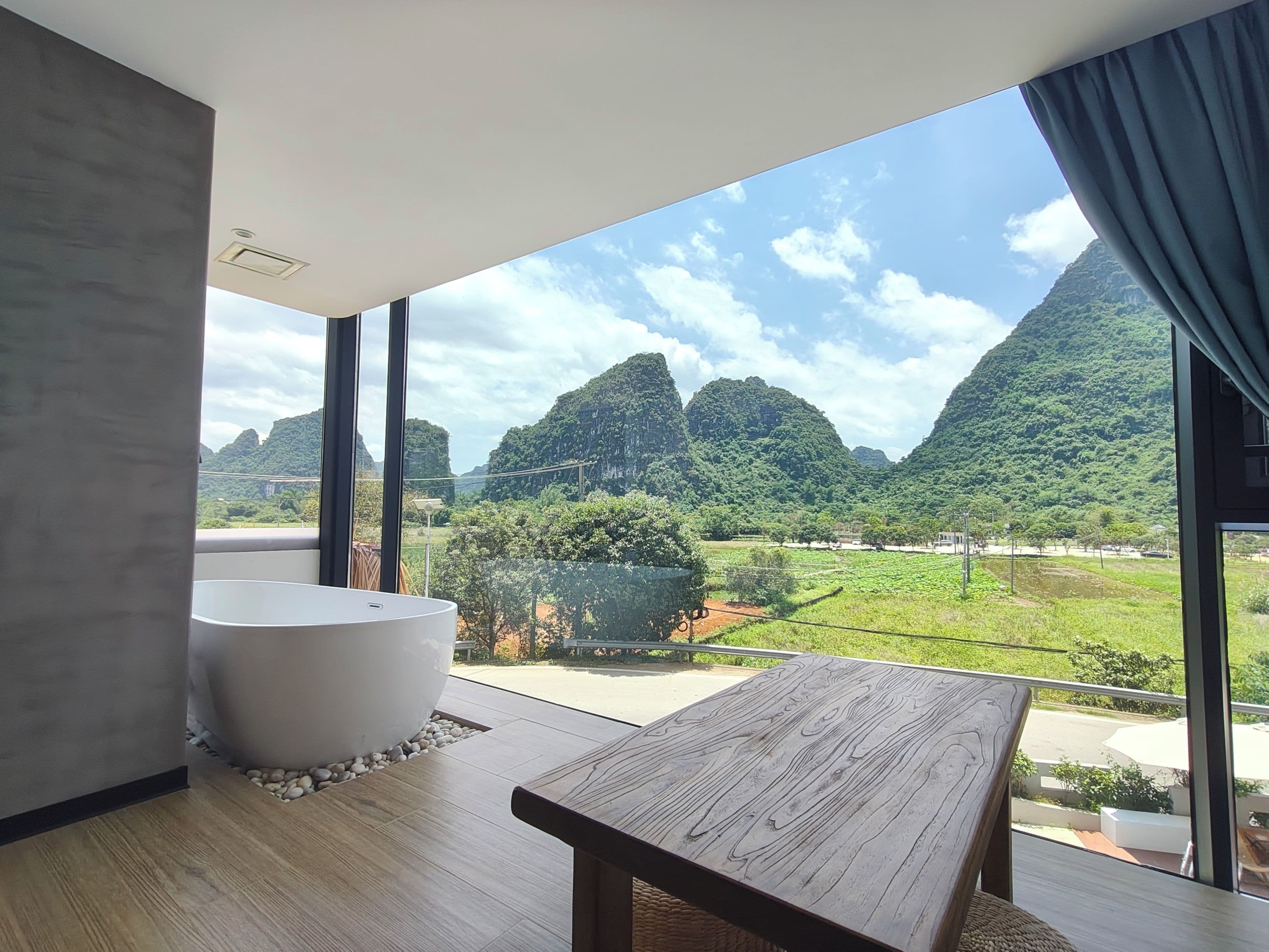 A modern bathroom with a large bathtub, a wooden bench, and a view of a mountainous landscape through large windows.