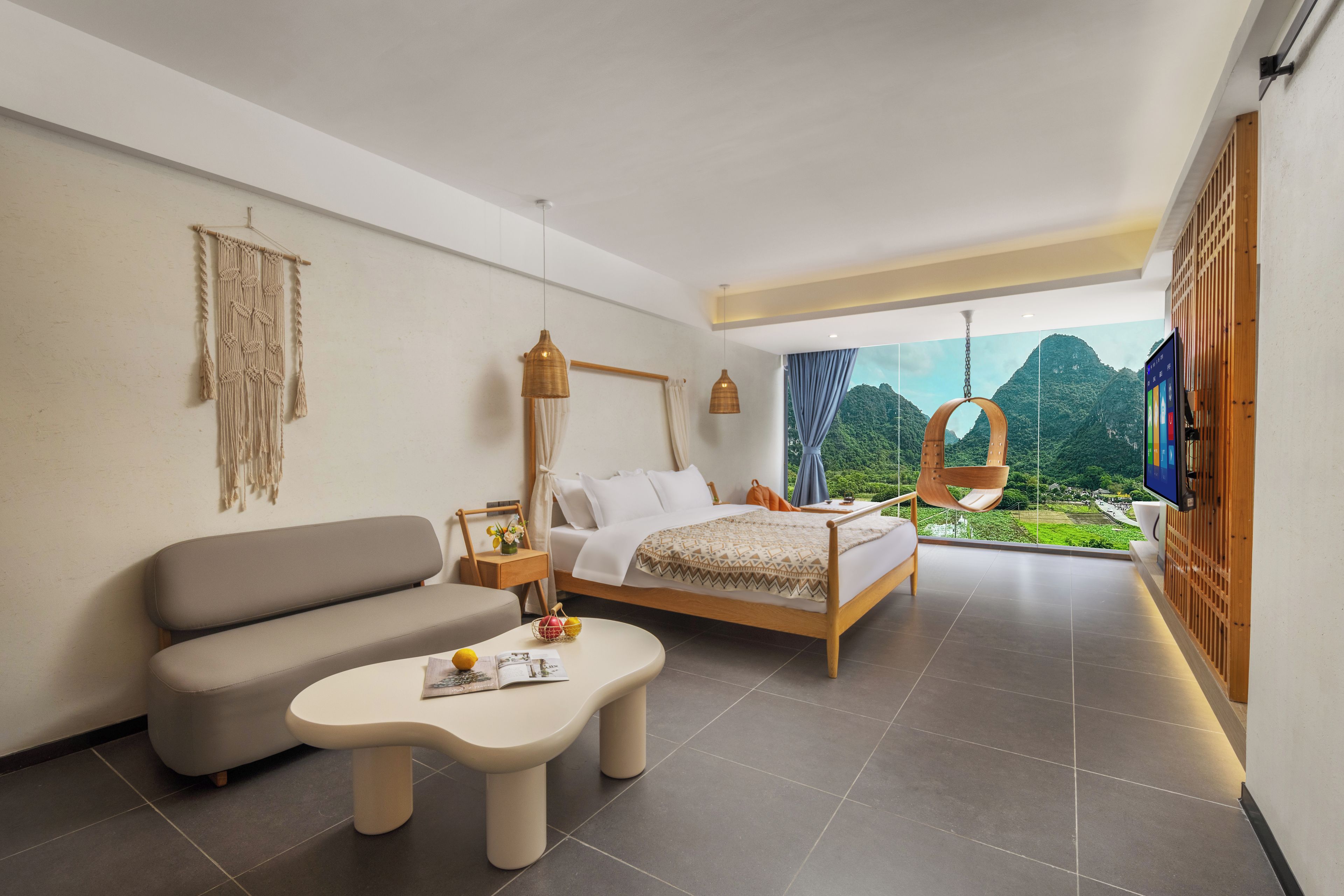 A modern bedroom with a bed, sofa, and a small table. There is a view of greenery outside the window.