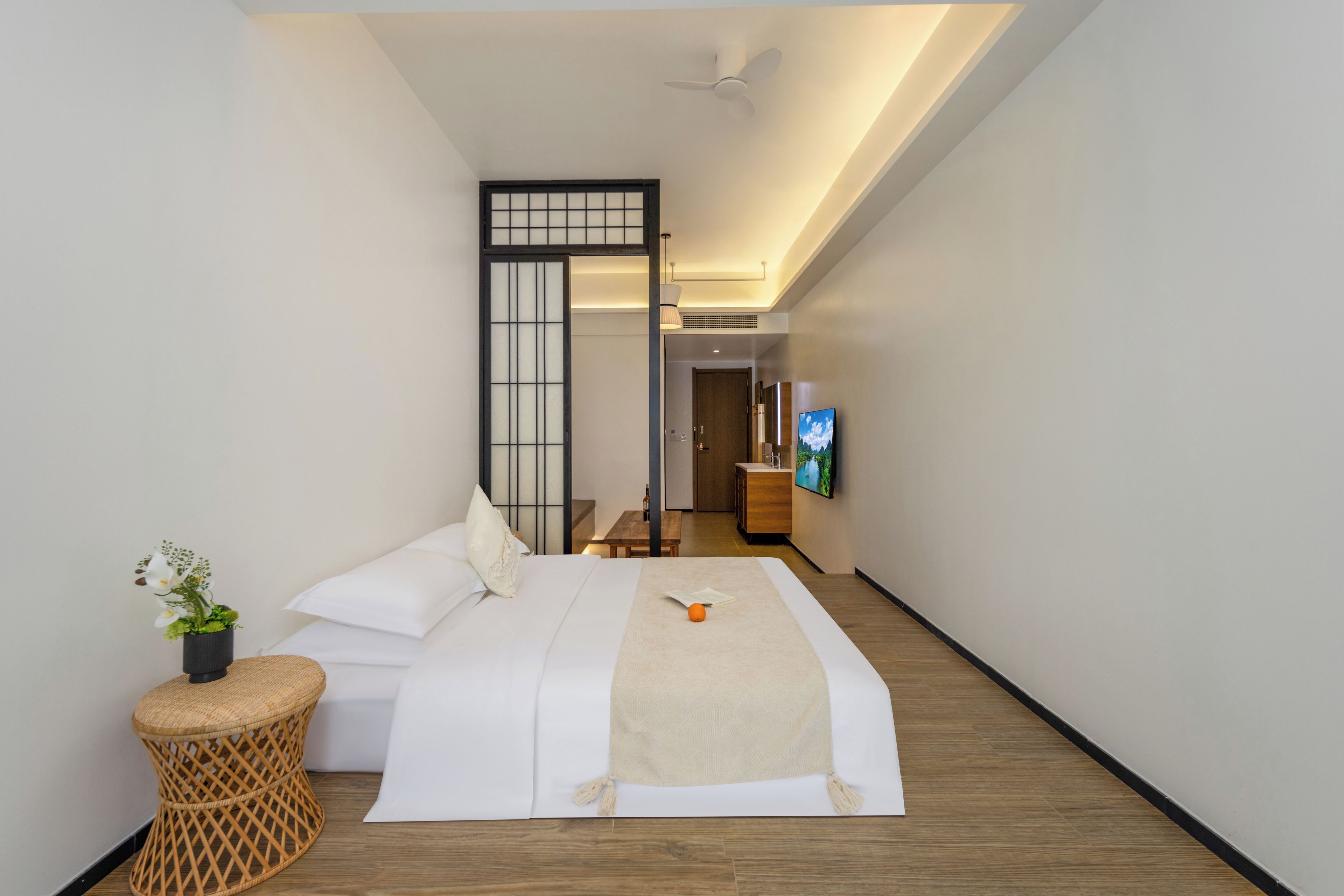 Habitación de hotel con cama, una mesita, televisor y una planta decorativa.