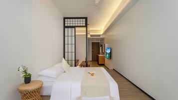 Habitación de hotel con cama, una mesita, televisor y una planta decorativa.