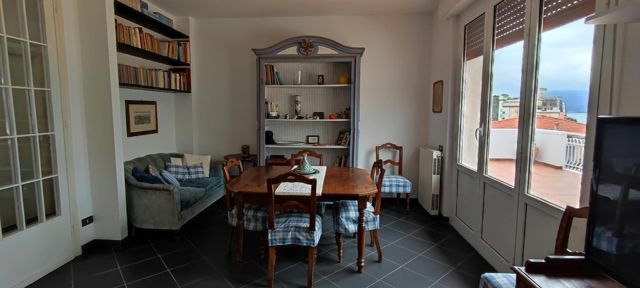 Un accogliente soggiorno con tavolo da pranzo, sedie, divano, libreria e vista dalla finestra.