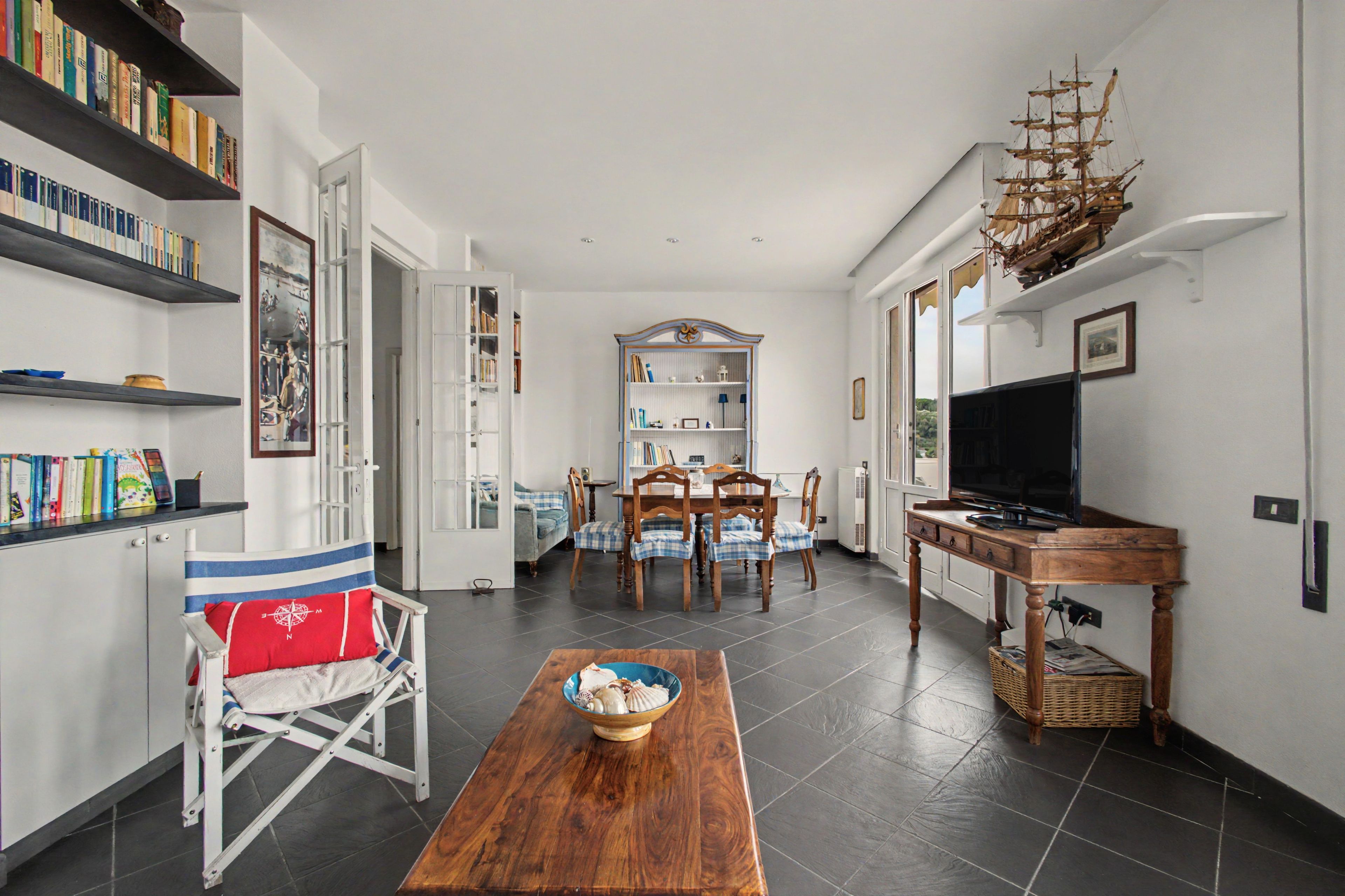 A modern living room with a wooden dining table, a television, and a bookshelf filled with books.
