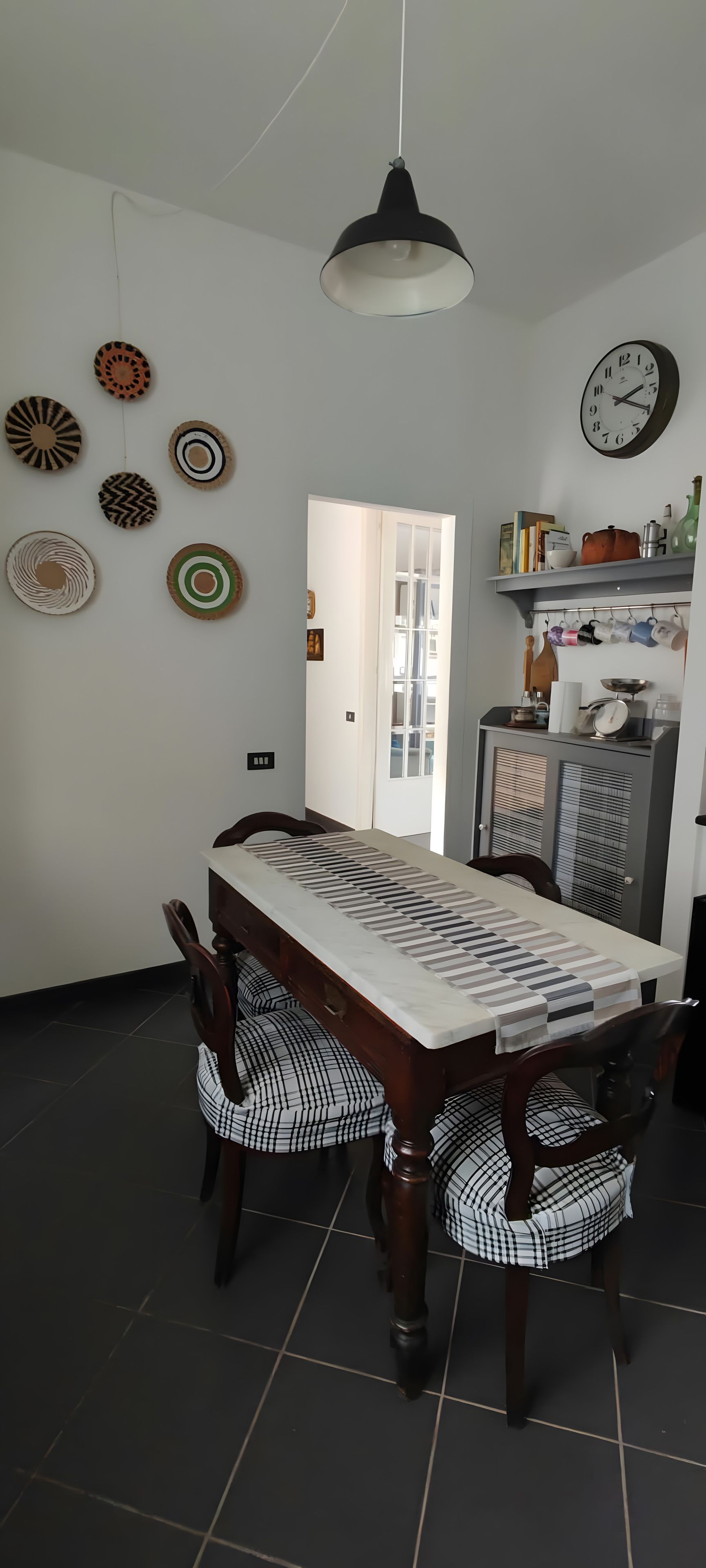 Zona pranzo con tavolo e sedie in legno, lampadario e piastre decorative a parete.