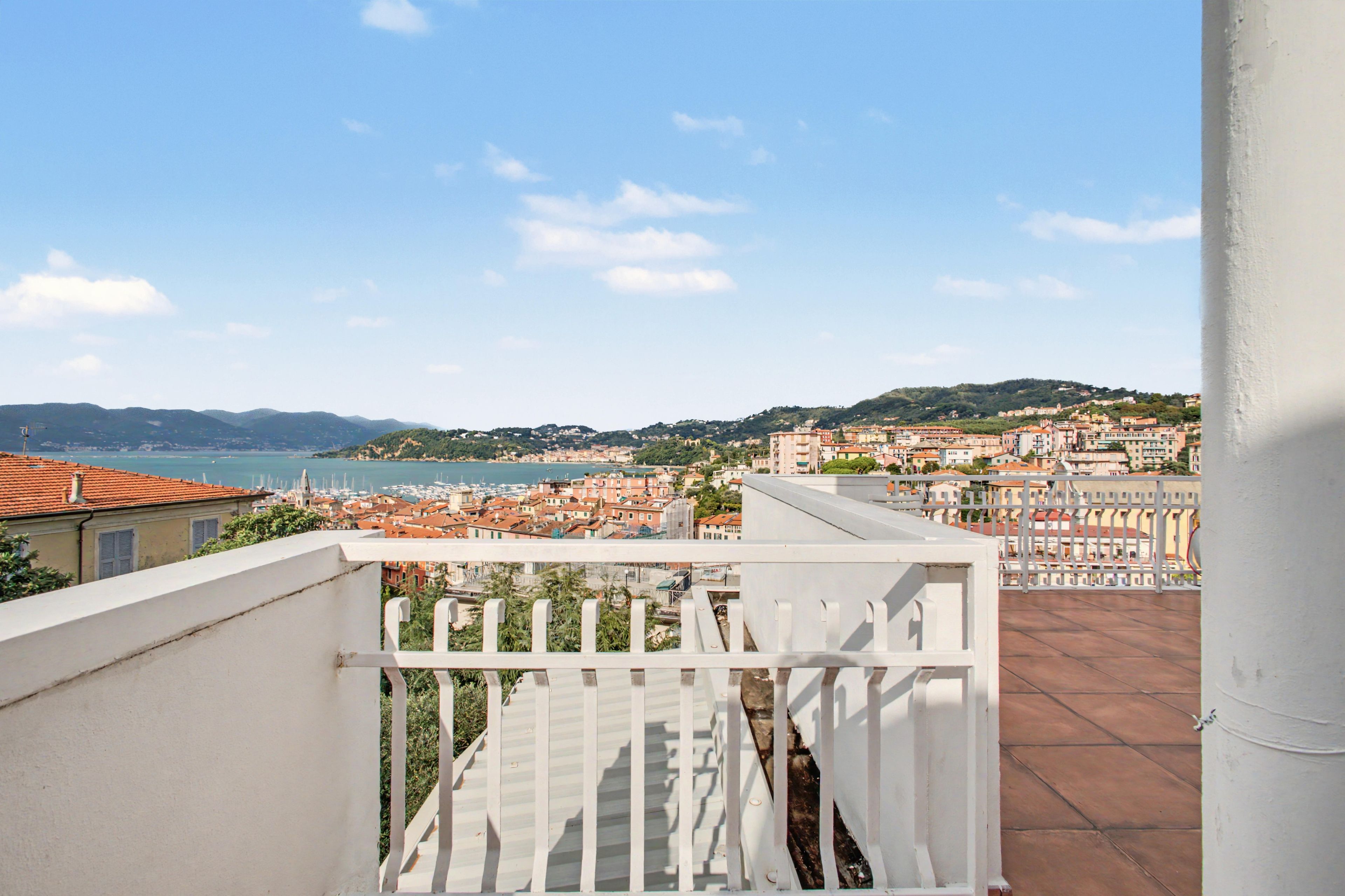 Un balcone con vista su una località costiera, cielo sereno e montagne in lontananza.