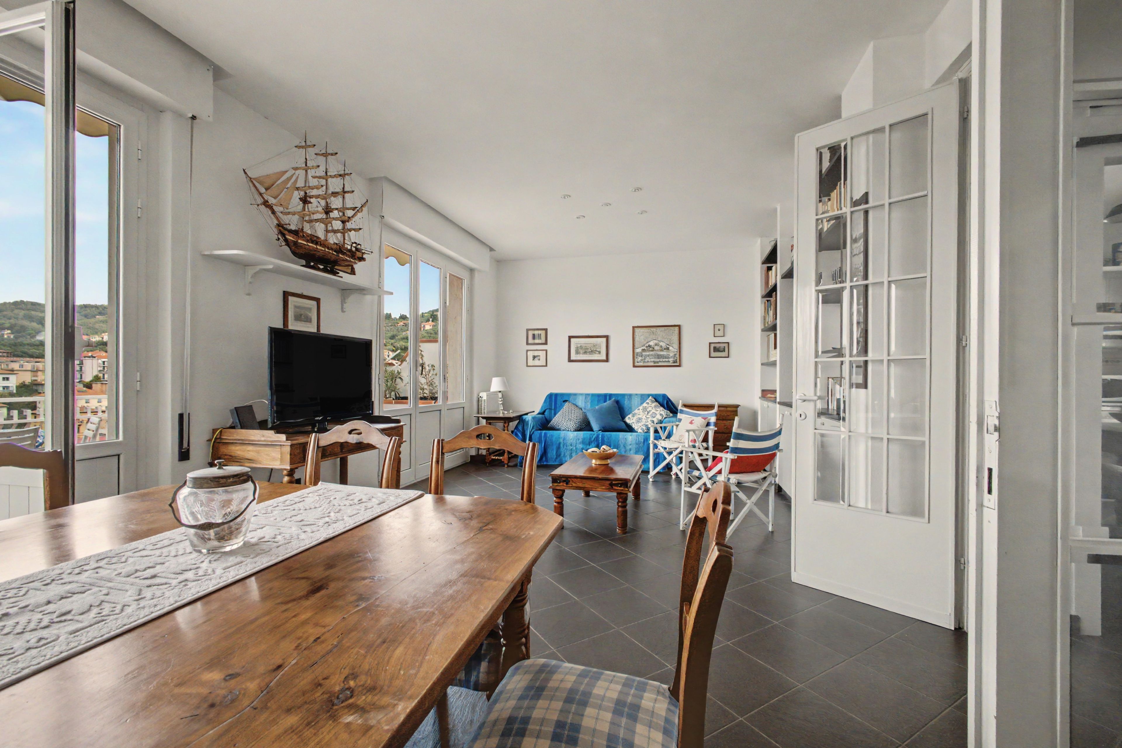 Un'ampia zona giorno con un tavolo da pranzo in legno, un divano blu e un modellino di nave appeso al muro.