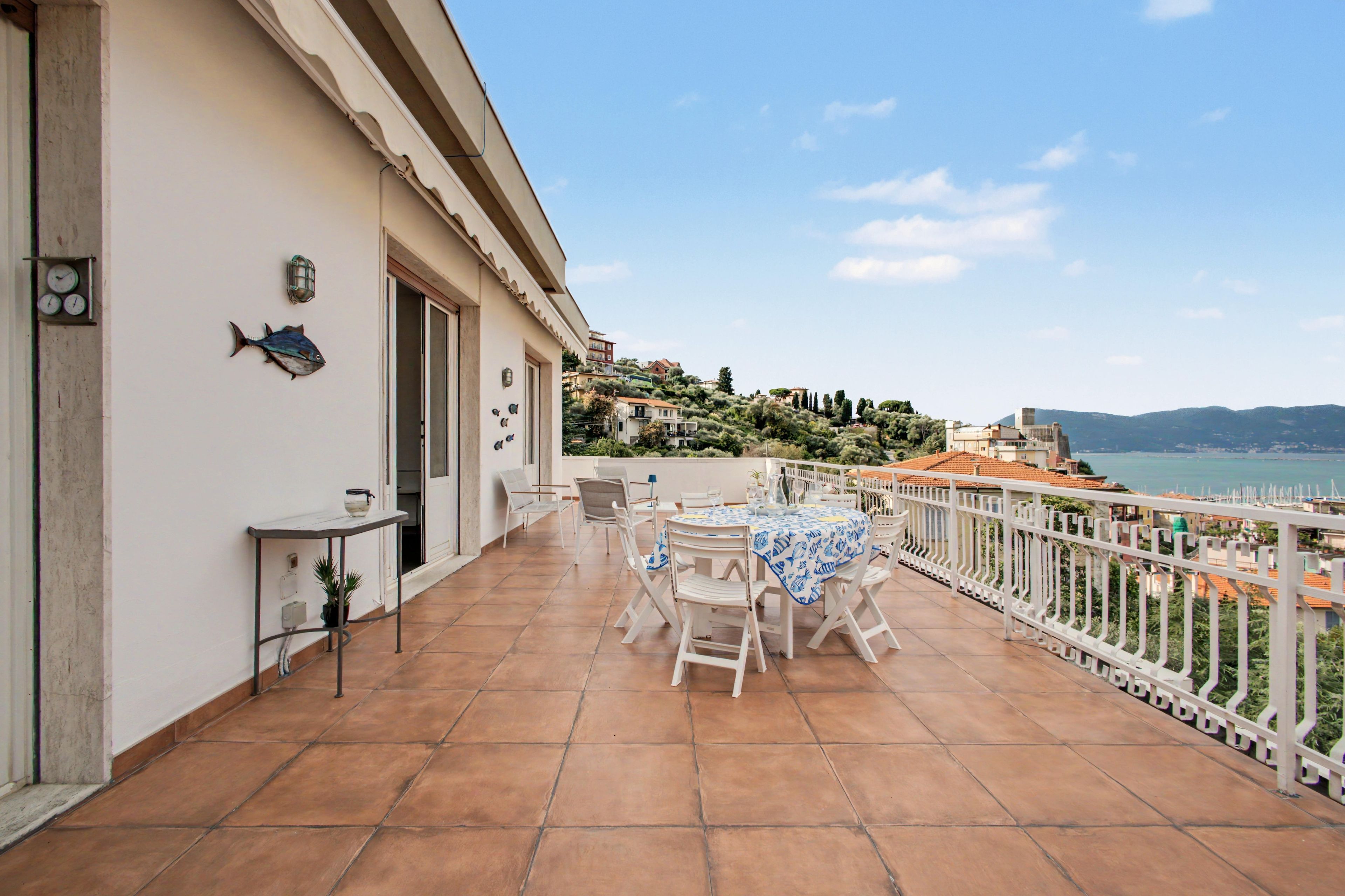 Una terrazza con tavolo e sedie, una decorazione a forma di pesce e vista sul mare e sulle colline.