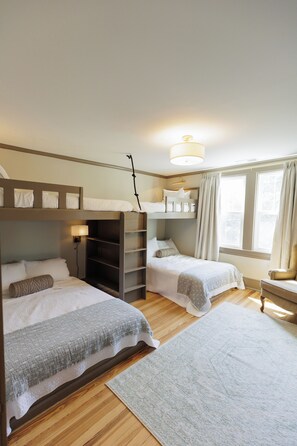 Ein Schlafzimmer mit zwei Etagenbetten, einem Nachttisch mit Lampe, einem Sessel und einem Fenster mit Vorhängen.
