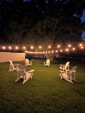 An outdoor seating area with Adirondack chairs and string lights. -  Spacious 4-Bedroom Group and Family Retreat: Game Room, Bunk Room, Walk2Shops (Matthews)