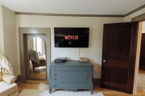 Ein Zimmer mit an der Wand montiertem Fernseher, der 'NETFLIX' zeigt, einem Schrank mit Schubladen, einer Tür und einem Spiegel, der einen Teil des Raumes widerspiegelt.