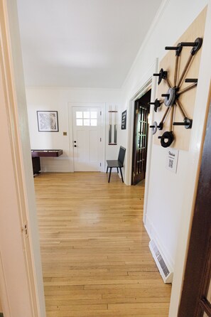 Ein Zimmer mit Holzboden, einer weißen Tür, einem Stuhl und einem an der Wand befestigten Ablagefach mit diversen Gegenständen.