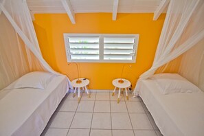 Ein Zimmer mit zwei Betten, einem Fenster mit Jalousien und einem kleinen Tisch mit einer Lampe.