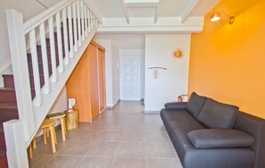 A living room with a grey sofa, a staircase with white railings, and a wooden door. - Duplex Papaye Deshaies. Sea view. Swimming pool (Deshaies)
