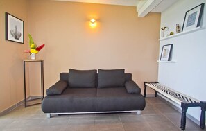 A modern living room with a dark grey sofa, a small side table with a vase of flowers, and a bench with a geometric pattern. - Copy of Duplex Papaye Deshaies. Sea view. Swimming pool (Deshaies)