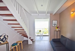 A modern living room with a staircase, a sofa, a small table with books, and a balcony with outdoor furniture. - Copy of Duplex Papaye Deshaies. Sea view. Swimming pool (Deshaies)