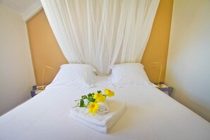 Una habitación de hotel con una cama, cortinas blancas, dos mesitas de noche y una toalla con flores.