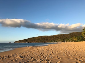 A beach with footprints, a clear sky, and a forested hill in the background. - Copy of Duplex Papaye Deshaies. Sea view. Swimming pool (Deshaies)